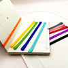 A collection of colorful silicone elastic rubber bands laid out on a spiral notebook page.