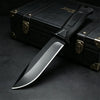 A black full tang fixed blade knife rests on a dark surface next to a black leather box.