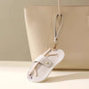 A light beige leather handbag with a white Lychee pattern eyeglasses case attached to the strap.