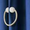 Goldfarbener geflochtener Ring mit Perlenakzenten als magnetischer Vorhangclip auf dunkelblauer Stoff.