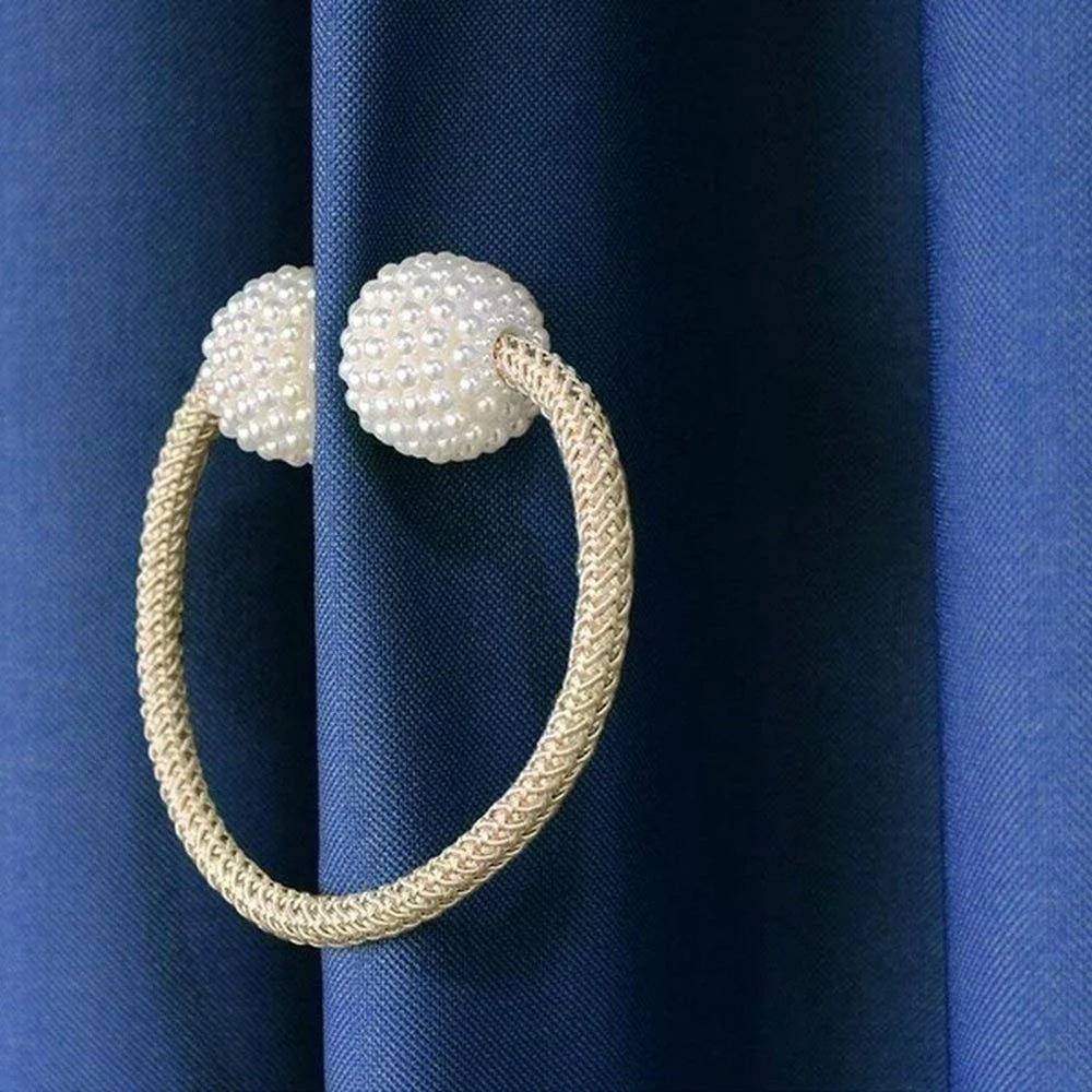 Goldfarbener geflochtener Ring mit Perlenakzenten als magnetischer Vorhangclip auf dunkelblauer Stoff.