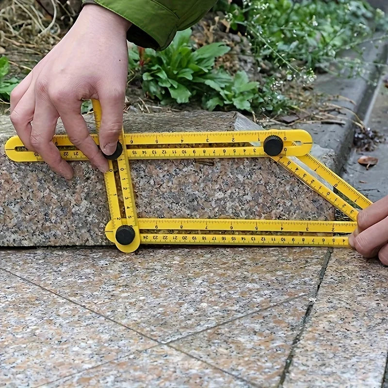 A hand holds a yellow plastic measuring ruler against a stone surface, showing the markings and scale.