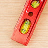 A red magnetic level ruler showing markings and measuring holes on a wooden surface.
