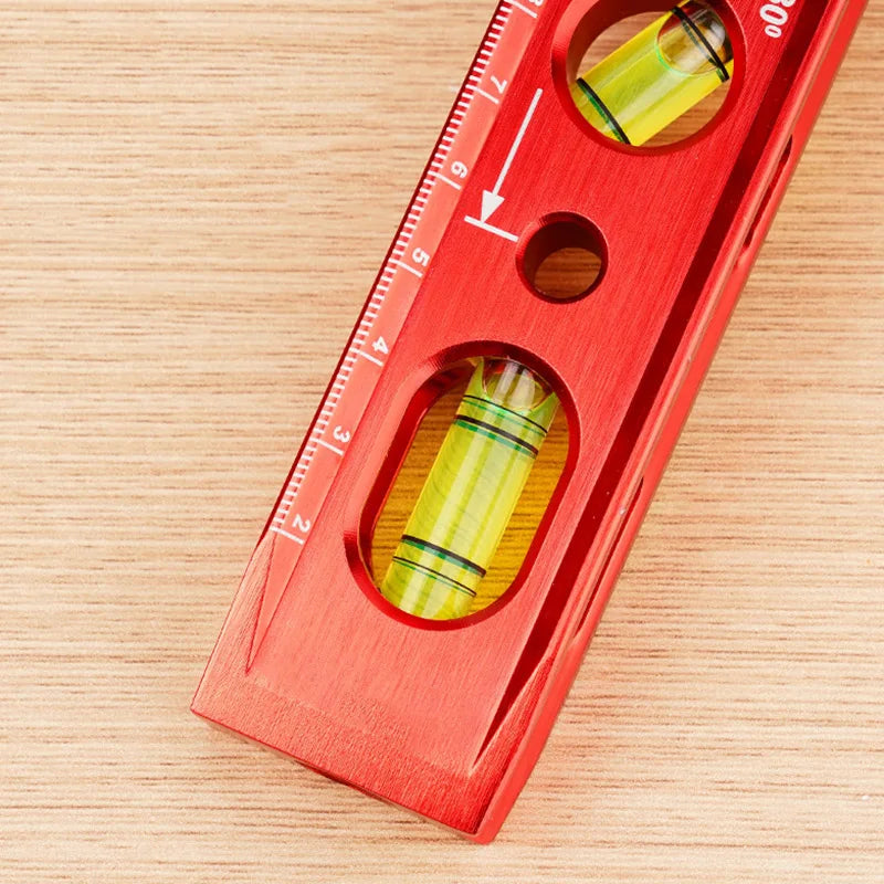 A red magnetic level ruler showing markings and measuring holes on a wooden surface.