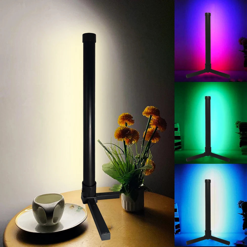 Lampe sur pied noire avec tête LED RGB à côté d'une tasse sur une table en bois, affichant différentes options de couleur.