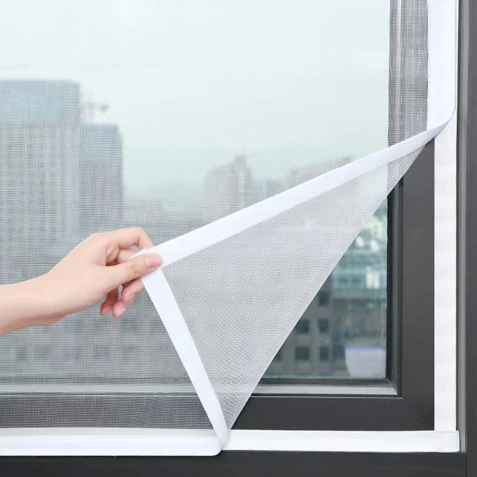 A hand is holding a white invisible zipper mosquito window screen against a dark window frame.