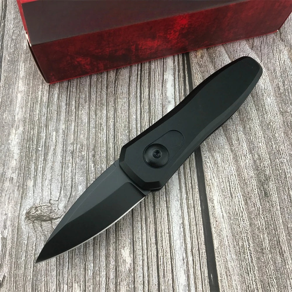 A black compact folding pocket knife with a visible blade is placed on a wooden surface next to a red box.