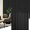 A dark vertical fluted wall panel in a modern interior setting with a chair and plant.