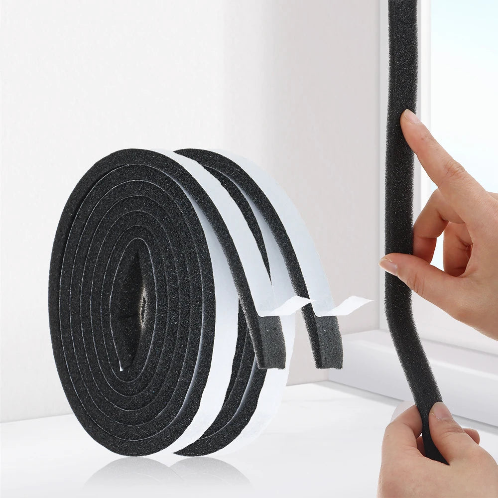 A hand is applying black self-adhesive foam weather stripping tape to a window frame.