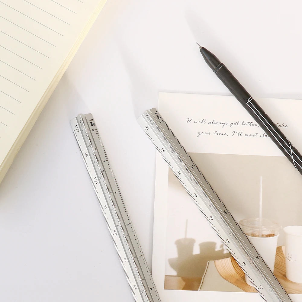 A close-up shot of a black pen and a silver aluminum triangular ruler on a white surface.