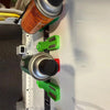 A close-up view of a magnetic spray can holder with green and silver components mounted on a white surface.