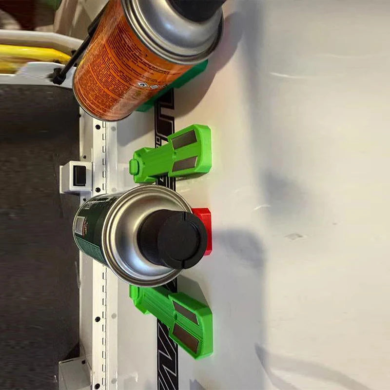 A close-up view of a magnetic spray can holder with green and silver components mounted on a white surface.
