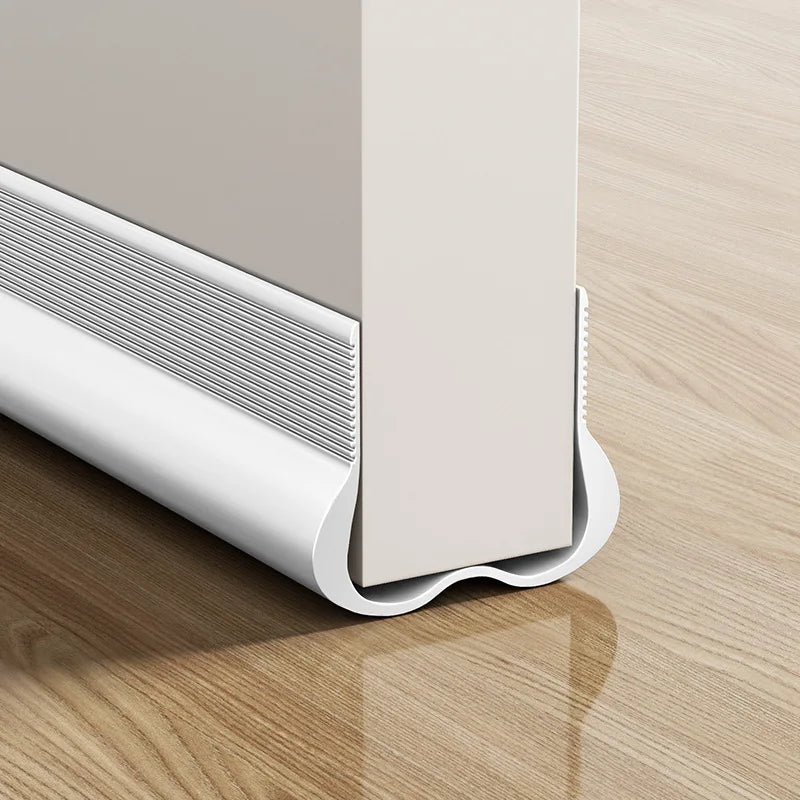 A white flexible PVC door draft stopper weather strip installed on a wooden surface.
