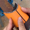 A hand holds an orange precision pipe saddle template, showing its shape and construction.
