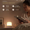 A woman is using an RGB ambient lighting touch switch lamp next to a book in a bedroom setting.