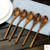 A set of natural wooden spoons and forks laid on a light blue napkin on a dark wooden surface.