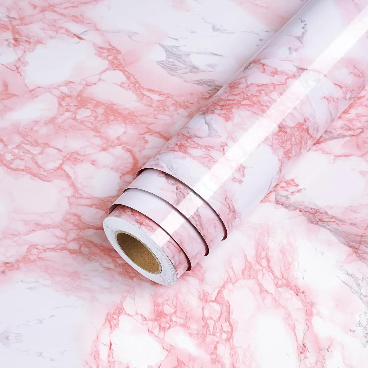 Roll of glossy pink marble contact paper lying on a white marble surface