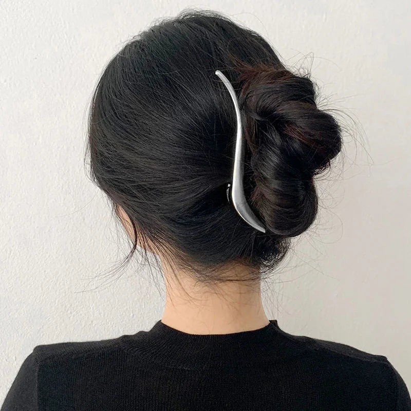 A woman's dark hair is styled in a bun using elegant gold S-shaped metal hair clips.