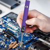 A hand holds a purple portable mini soldering iron kit, pointing the tip at a blue electronic circuit board.