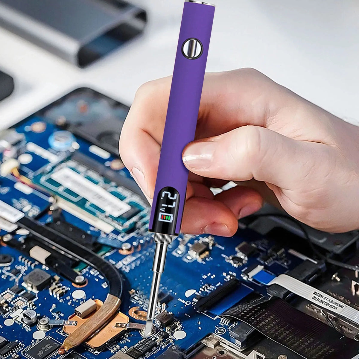 A hand holds a purple portable mini soldering iron kit, pointing the tip at a blue electronic circuit board.