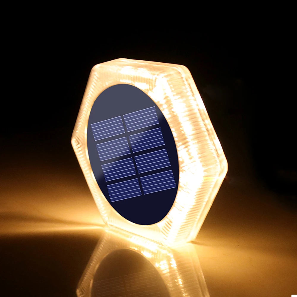 Sechseckige Solarlampe mit dunkler Platte und blauen Solarzellen, beleuchtet auf einer reflektierenden Oberfläche.