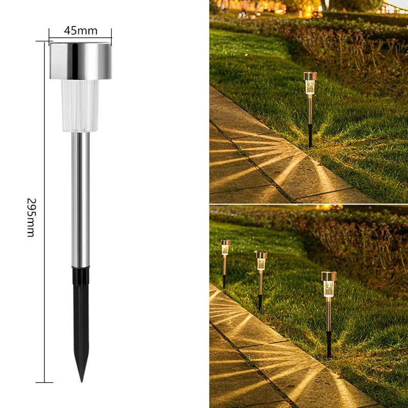 A silver and black solar powered outdoor garden lantern with a pointed tip, shown in a grassy landscape.