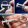 A hand holds a precision metal jewelry measuring ruler and caliper keychain against a dark background.