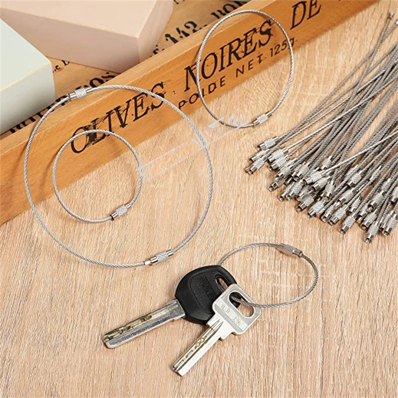 A set of stainless steel wire keychain tags and keys displayed on a wooden surface.