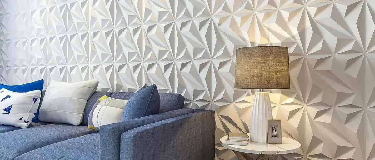 A gray sofa is positioned in front of a textured, geometric white wall panel design with a lamp on a side table.