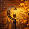 A solar moon light with an owl decoration casting shadows on a brick wall.