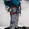 A person wearing gray pants and a teal shirt is equipped with parachute rope work gear outdoors.