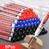 A collection of red and white long nib marker pens with black tips arranged in a pile on a wooden block.