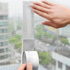 A hand is shown applying or inspecting a strip of mesh window screen repair tape against a window pane.