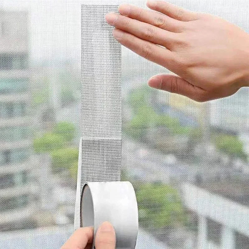A hand is shown applying or inspecting a strip of mesh window screen repair tape against a window pane.
