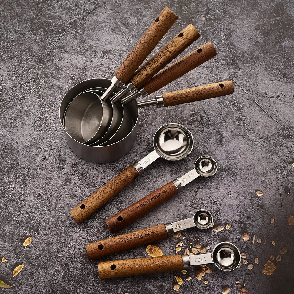 A set of stainless steel and wooden measuring spoons arranged on a dark gray surface.