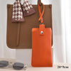 An orange PU leather eyeglasses case hanging from a brown tote bag with a checkered fabric detail.