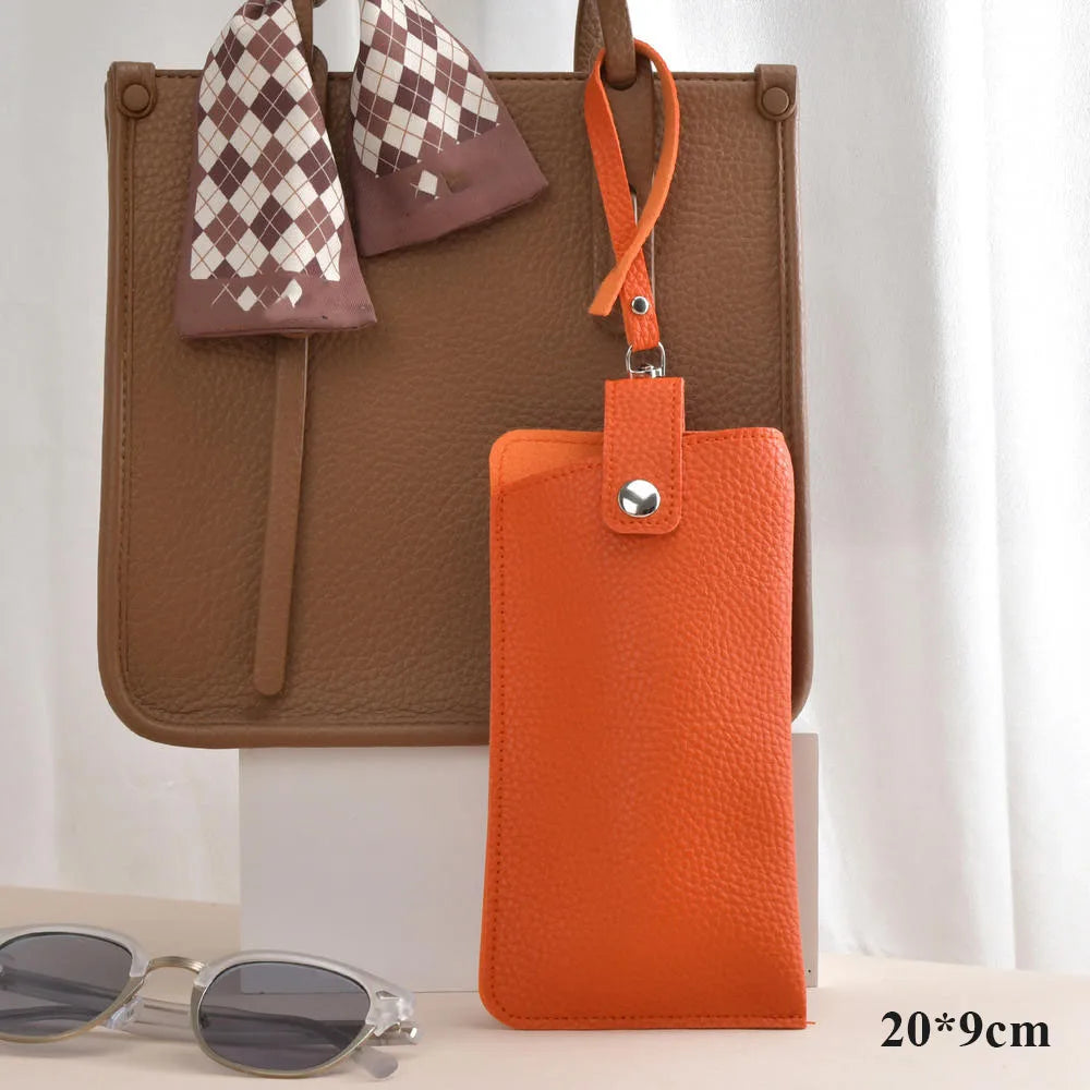 An orange PU leather eyeglasses case hanging from a brown tote bag with a checkered fabric detail.
