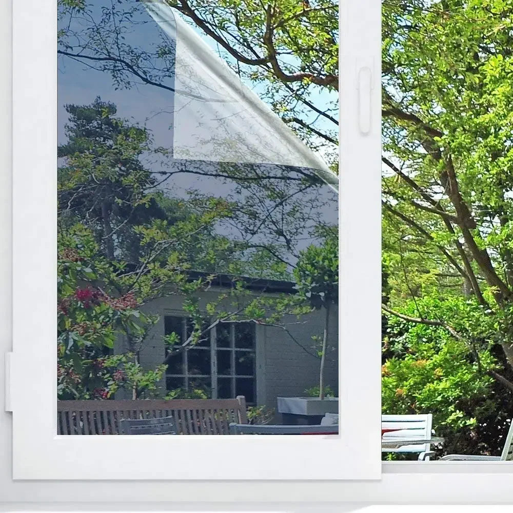 Gros plan d'un cadre de fenêtre blanc avec un panneau de film miroir unidirectionnel montrant des arbres et feuillage verts l