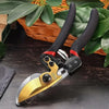 A pair of professional metal pruning shears with black handles and gold accents resting on a dark wooden surface amidst green