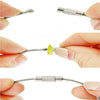 A set of stainless steel wire keychain tags, showing various wire shapes and a yellow tag being held by fingers.