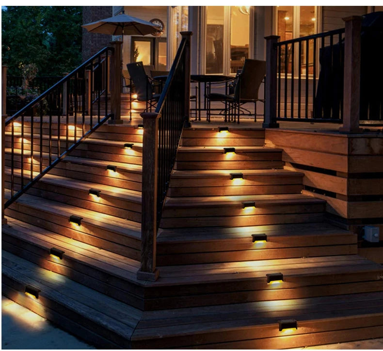 Exterior view of wooden stairs illuminated by ground-level solar LED lights leading to a deck and outdoor seating area.