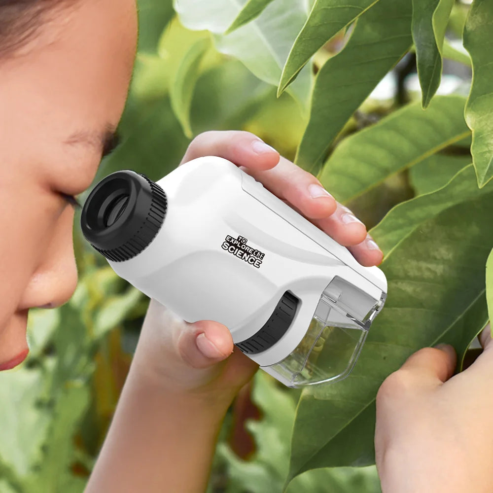 A child holds a white handheld educational microscope for kids against a blurred green leaf background.