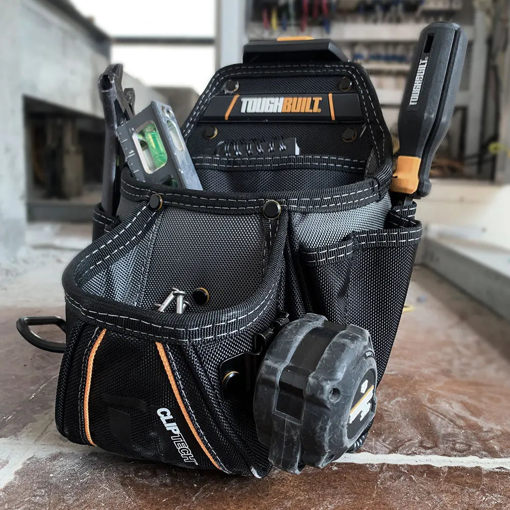 A black heavy-duty construction tool pouch with a rugged clip and storage compartments is shown on a wooden surface.