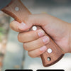 A hand holds a solid wood handle axe with triple rivets, showing the grip and blade design.
