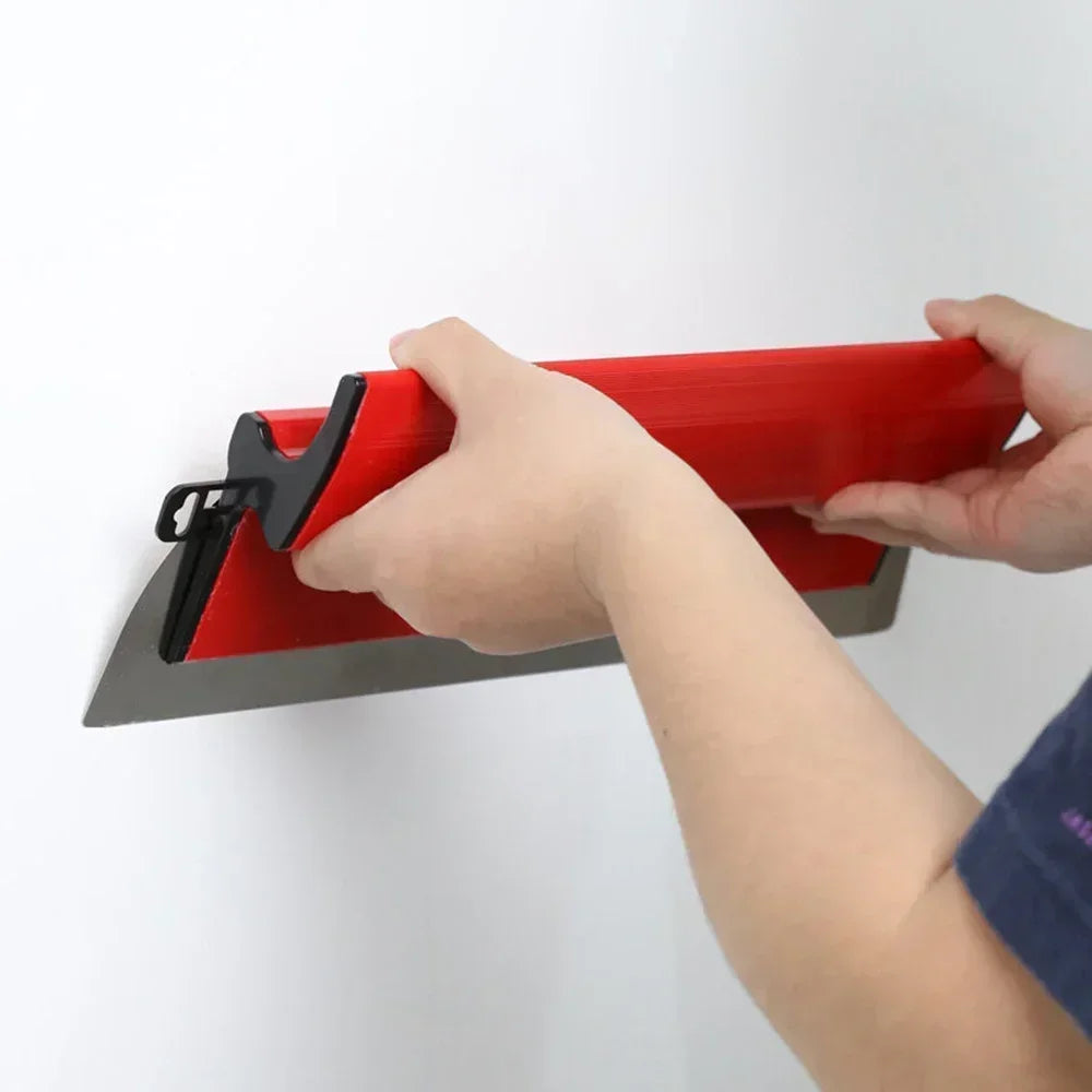 A hand is holding a red and gray professional skimming blade against a white wall.