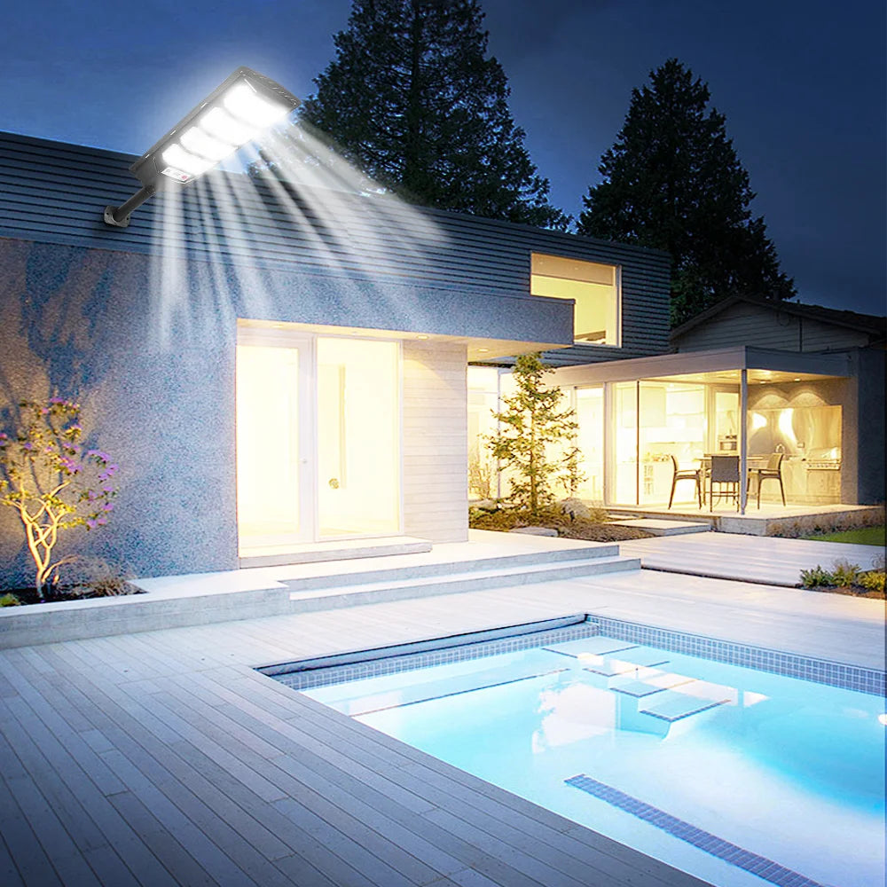 An outdoor solar motion sensor LED light illuminates a modern house and swimming pool at night.