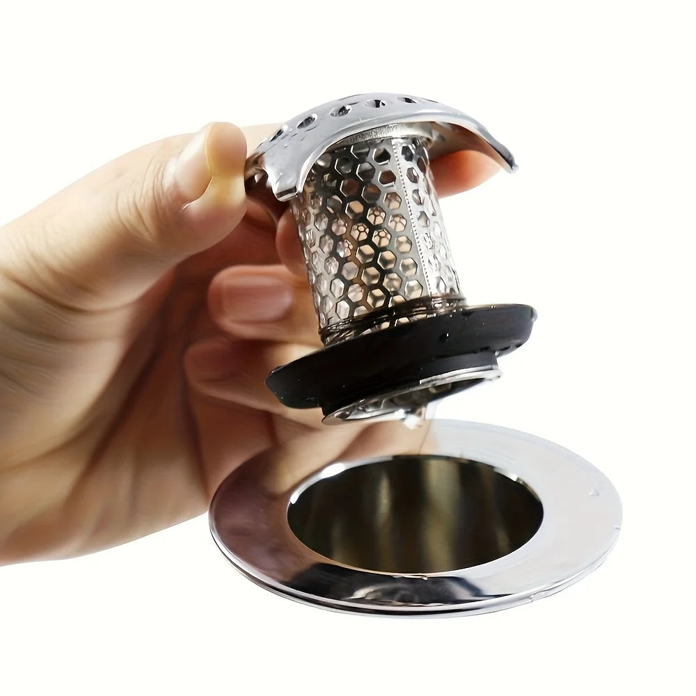 A hand holds a stainless steel bathtub drain with a mesh hair catcher over a circular drain plate.