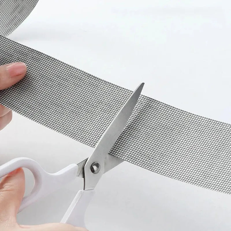 A hand is using scissors to cut a strip of gray self-adhesive repair tape for window screens.