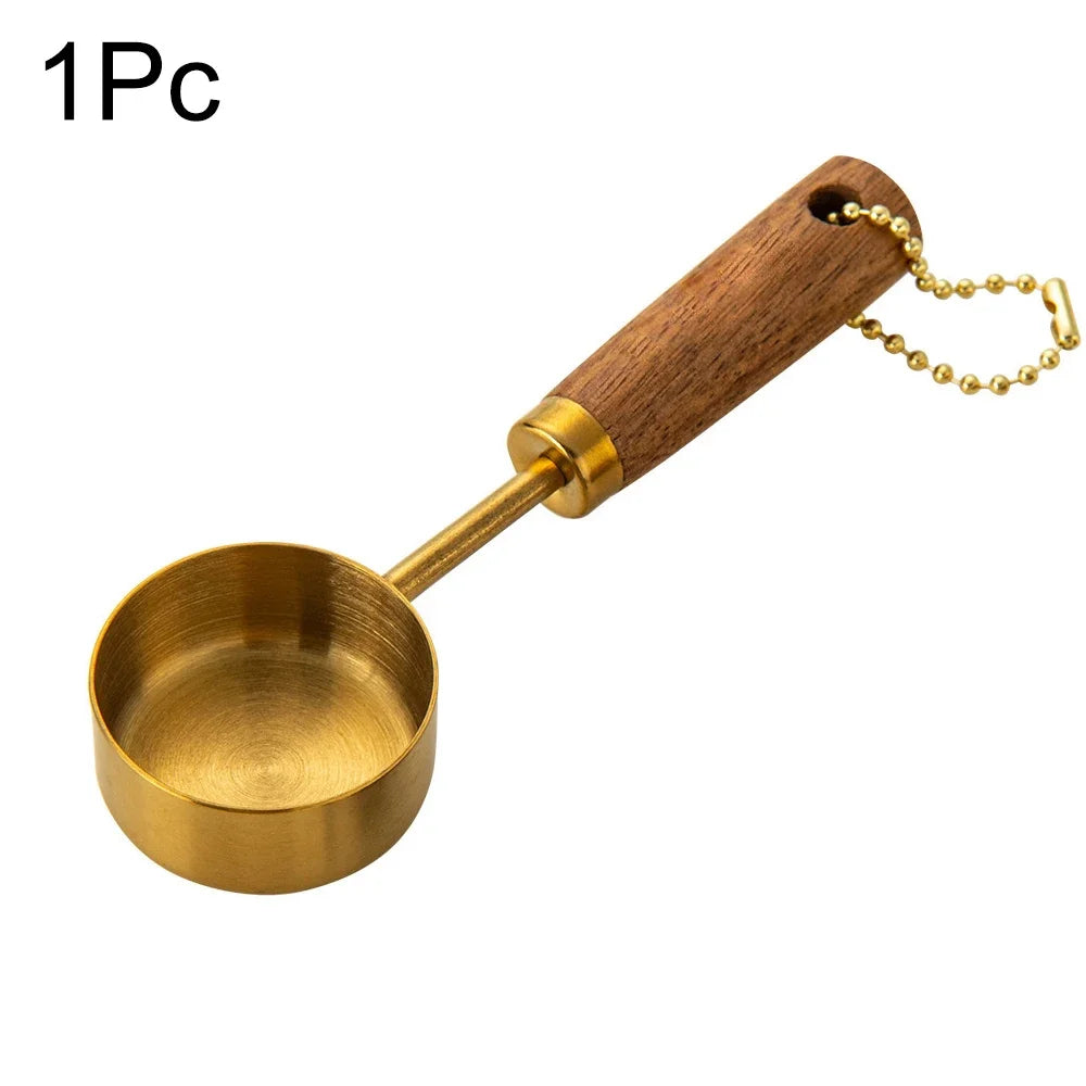 A single stainless steel measuring spoon with a wooden handle and gold-colored chain.