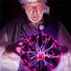 An elderly man with a white beard holds a glowing purple and pink plasma ball light.